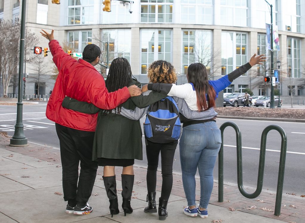 A photo of the backs of a group of students standing on a street.
